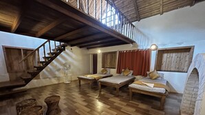 A cozy loft-style room with a wooden staircase, two beds, a fan, and a brick fireplace.