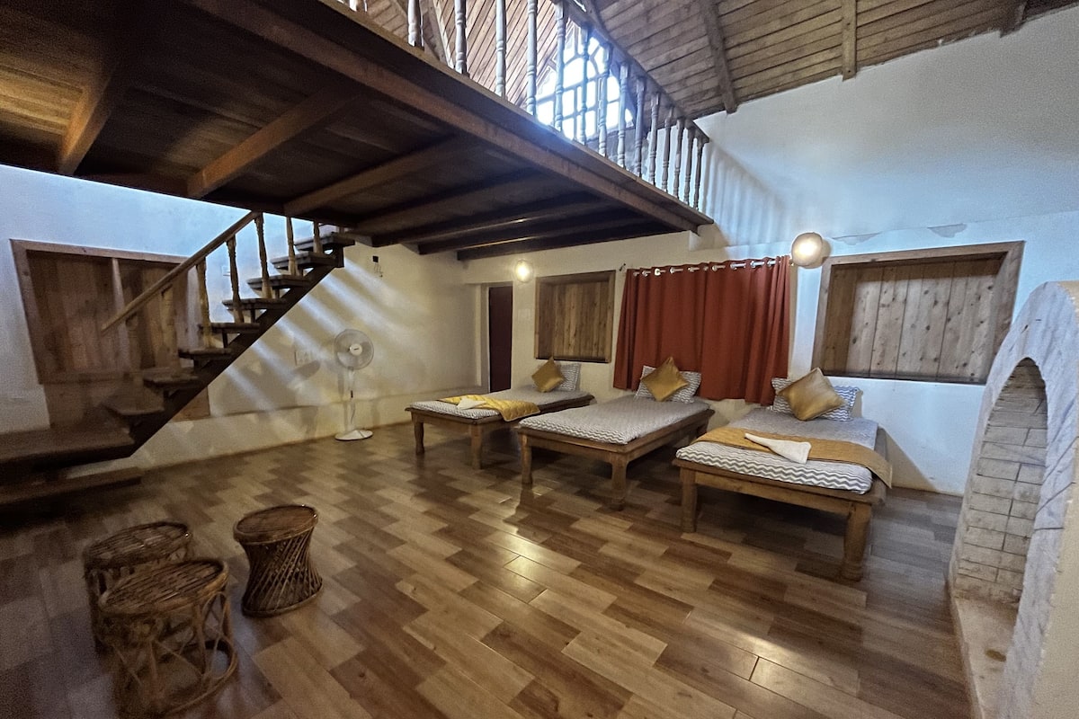 A cozy loft-style room with a wooden staircase, two beds, a fan, and a brick fireplace.