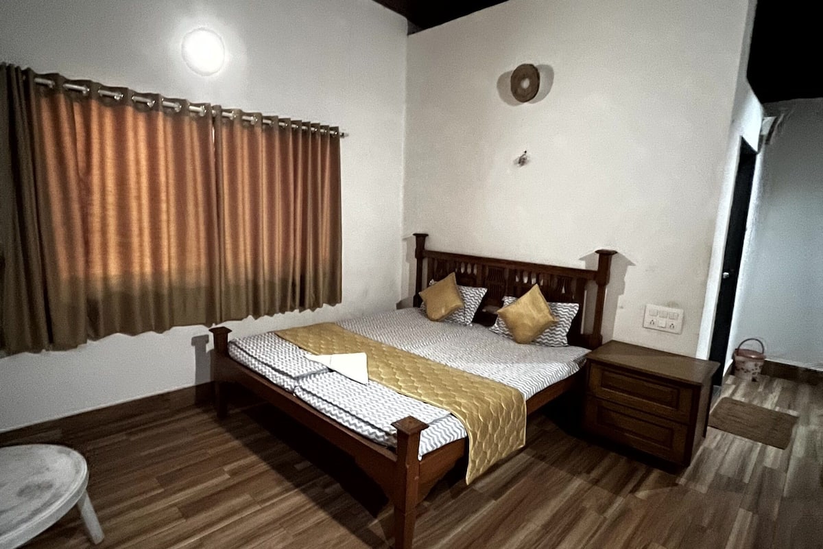 A bedroom with a wooden bed, a bedside table, a small round table, and a window with curtains.