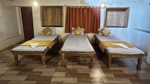 A room with three wooden beds arranged in a row, wooden floors, and a sloped ceiling with exposed beams.