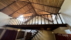 A wooden ceiling with a balcony railing, a staircase, and a window allowing natural light.