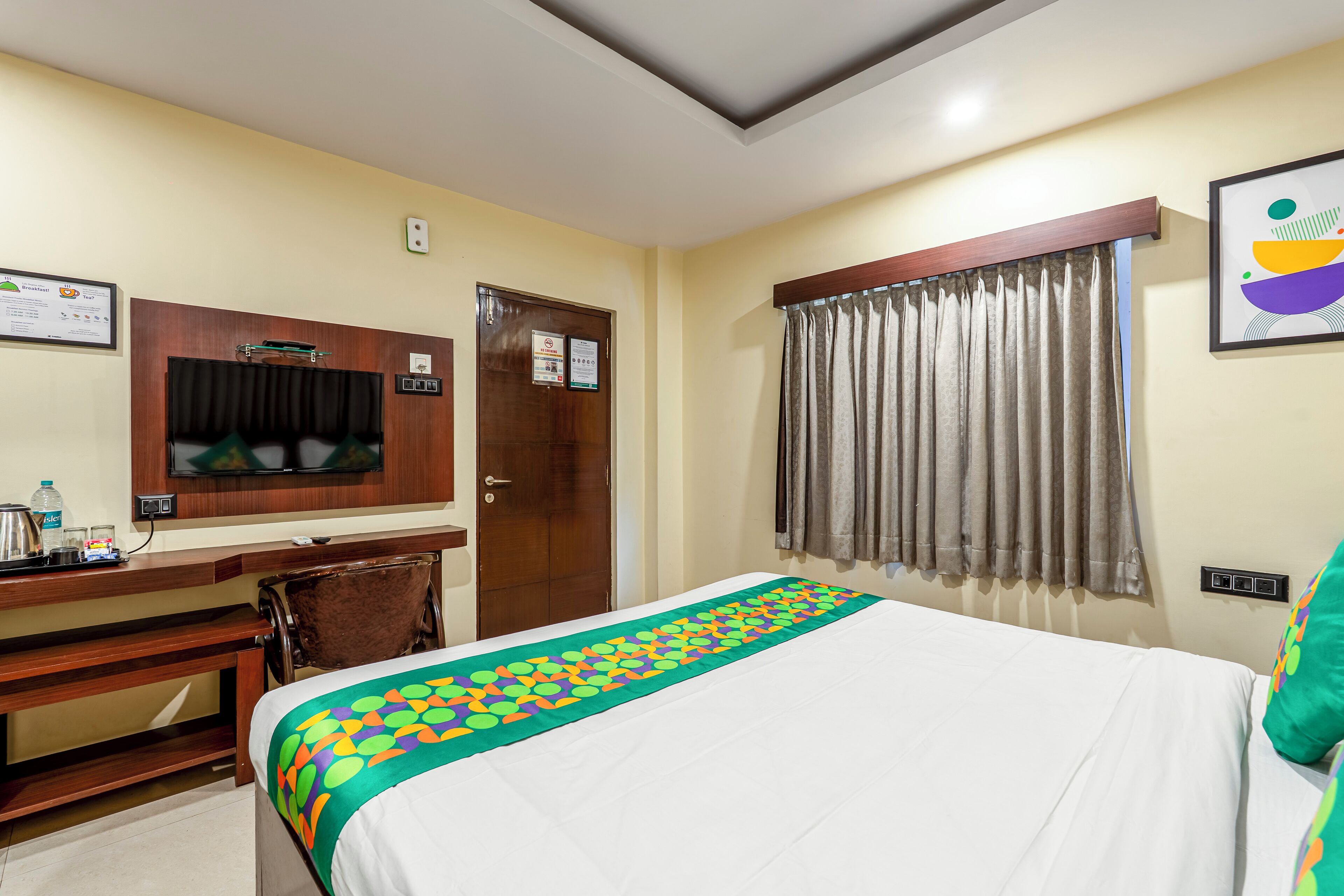 A hotel room with a bed, a desk, a chair, a television, and a window with curtains.