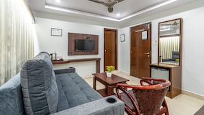 A living room with a grey sofa, a small table with a plant, a red chair, a television mounted on the wall, and a ceiling fan. - Treebo Marina Grand, Railway Station (Visakhapatnam)