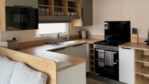 A compact kitchen with a microwave, stove, and sink, wooden cabinets, and a 'No Smoking' sign. - The Springer Van - Beautiful, luxury static (Aberlour)