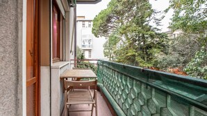 A balcony with a wooden table and chairs, a green patterned railing, and a view of trees and buildings.