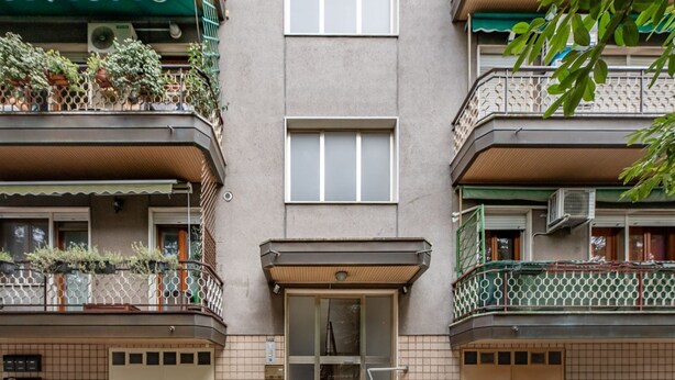 A multi-story building with a central entrance, balconies with plants, and tiled walls.