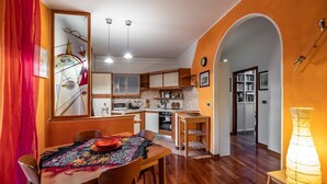 A compact kitchen with modern appliances, a dining area with a table and chairs, and an archway leading to a hallway with bookshelves.