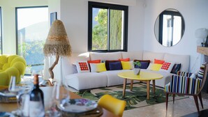 Ein modernes Wohnzimmer mit einem weißen Sofa, farbenfrohen Kissen, einem gelben Tisch und einem gestreiften Sessel.