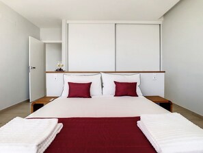 Une chambre d’hôtel avec un grand lit, deux tables de chevet, une tête de lit en bois et un coussin décoratif rouge.