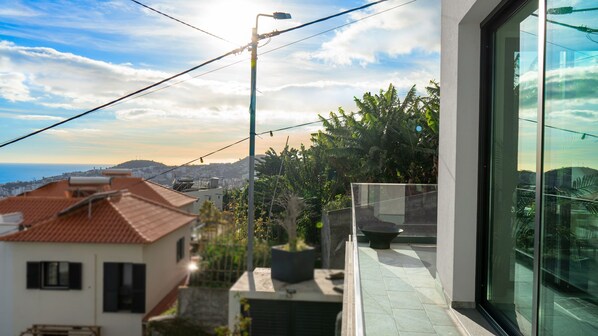 Un balcone con vista sulla città e sul mare, un edificio moderno con ampie finestre e un lampione.