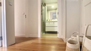 Ein Flur mit Holzboden, der zu einem Badezimmer mit Duschabtür aus Glas und einem weißen Waschbecken führt.