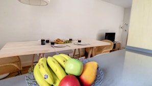 Ein Essbereich mit Tisch für zwei Personen, einer Obstschale mit Bananen und Äpfeln sowie einer hängenden Leuchte.