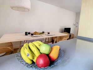 Ein Essbereich mit Tisch für zwei Personen, einer Obstschale mit Bananen und Äpfeln sowie einer hängenden Leuchte.
