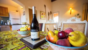 Une bouteille de vin, un saladier de fruits et une table recouverte d’une nappe à motifs.