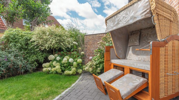 A wooden outdoor sofa with a canopy, positioned on a paved patio with a brick wall and lush greenery in the background. - Die Ferienwohnung Seute Deern in St. Peter-dorf für bis zu 2 Personen (St. Peter-Dorf)