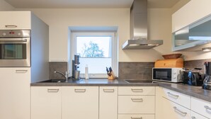 A modern kitchen with white cabinets, a built-in oven, a microwave, and a coffee machine. - Die Ferienwohnung Seute Deern in St. Peter-dorf für bis zu 2 Personen (St. Peter-Dorf)