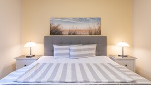 A neatly made bed with striped bedding, two bedside lamps, and a painting above the headboard. - Die Ferienwohnung Seute Deern in St. Peter-dorf für bis zu 2 Personen (St. Peter-Dorf)