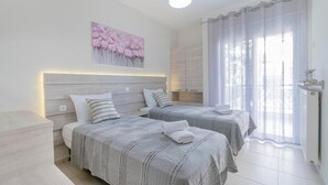 Ein modernes Schlafzimmer mit zwei Betten, einem großen Fenster mit transparenten Vorhängen und einem Wandbild.
