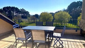 Eine Terrasse mit Tisch und Stühlen, einem Metallgeländer und Blick auf eine grüne Landschaft mit Bäumen.