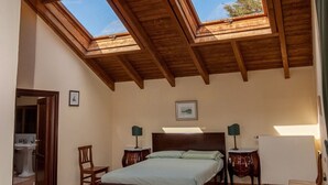 A bedroom with a wooden ceiling, skylights, a bed, two bedside tables, a chair, and a radiator. - Tenuta Cà dei Mandorli (Castel Boglione)