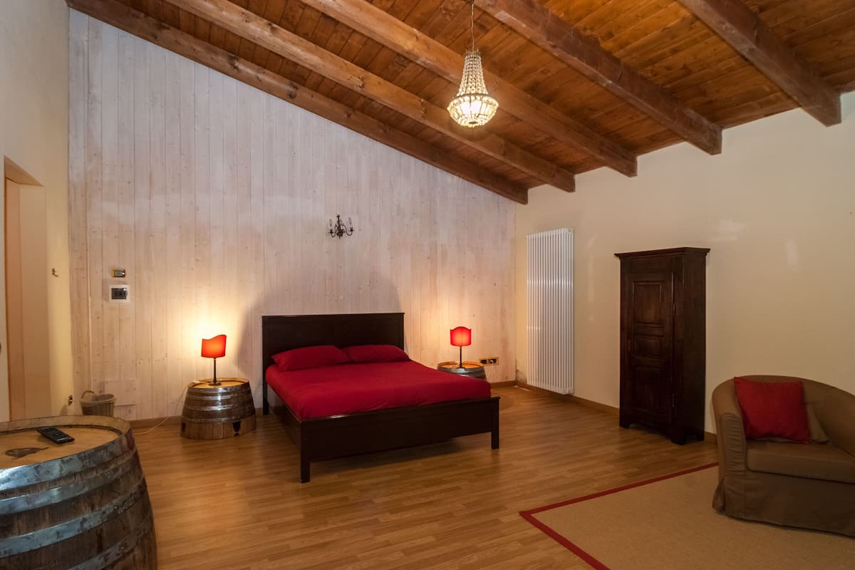 Ein Schlafzimmer mit Holzboden, einem Bett mit roter Bettwäsche, zwei Nachttischlampen, einem Holzschrank und einem Holzfass.