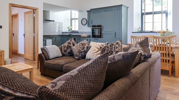 A modern living room with a sofa, a dining table, and a kitchen in the background.