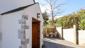 A white building with a stone facade, a wooden door, and a small outdoor seating area with wicker furniture.