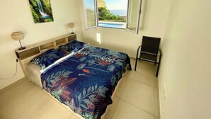 A bedroom with a bed, a nightstand, a lamp, a chair, and a window with a view of a pool and greenery.