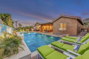 A swimming pool with lounge chairs, a barbecue area, and a building with a patio.