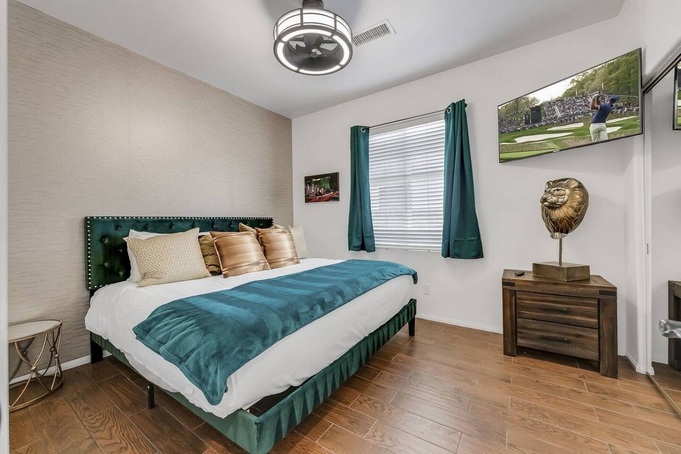 A bedroom with a bed, a bedside table, a wall-mounted TV, and a window with curtains.