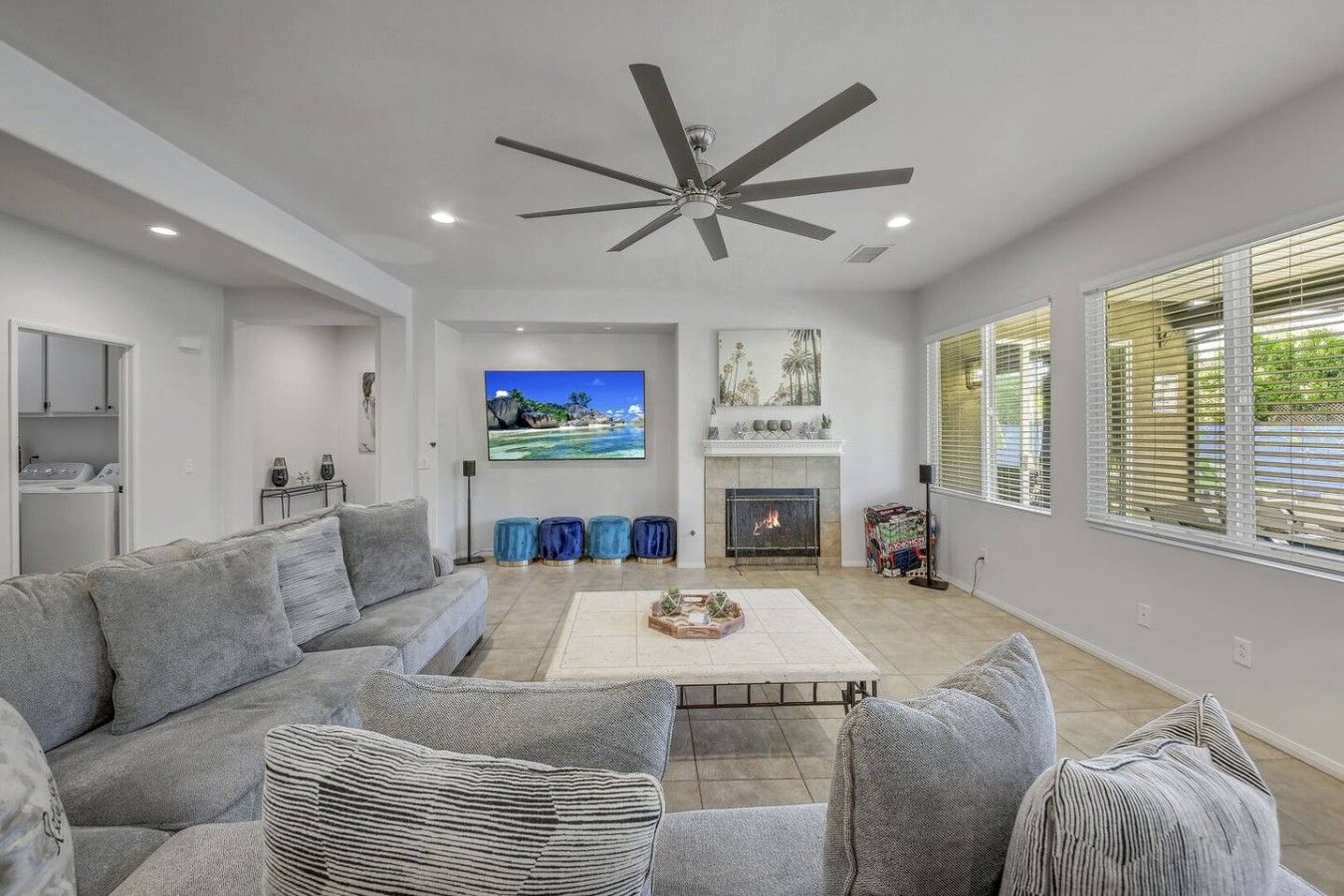 Una sala de estar moderna con un sofá gris, una chimenea, un televisor de pantalla plana y un ventilador de techo.