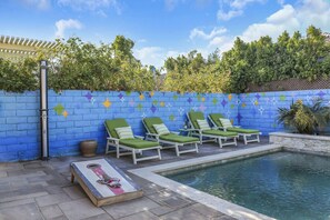 A pool area with lounge chairs and a blue wall with star patterns. - Stardust: Pool, Spa, FirePit, BBQ, EV Charger! (Indio)