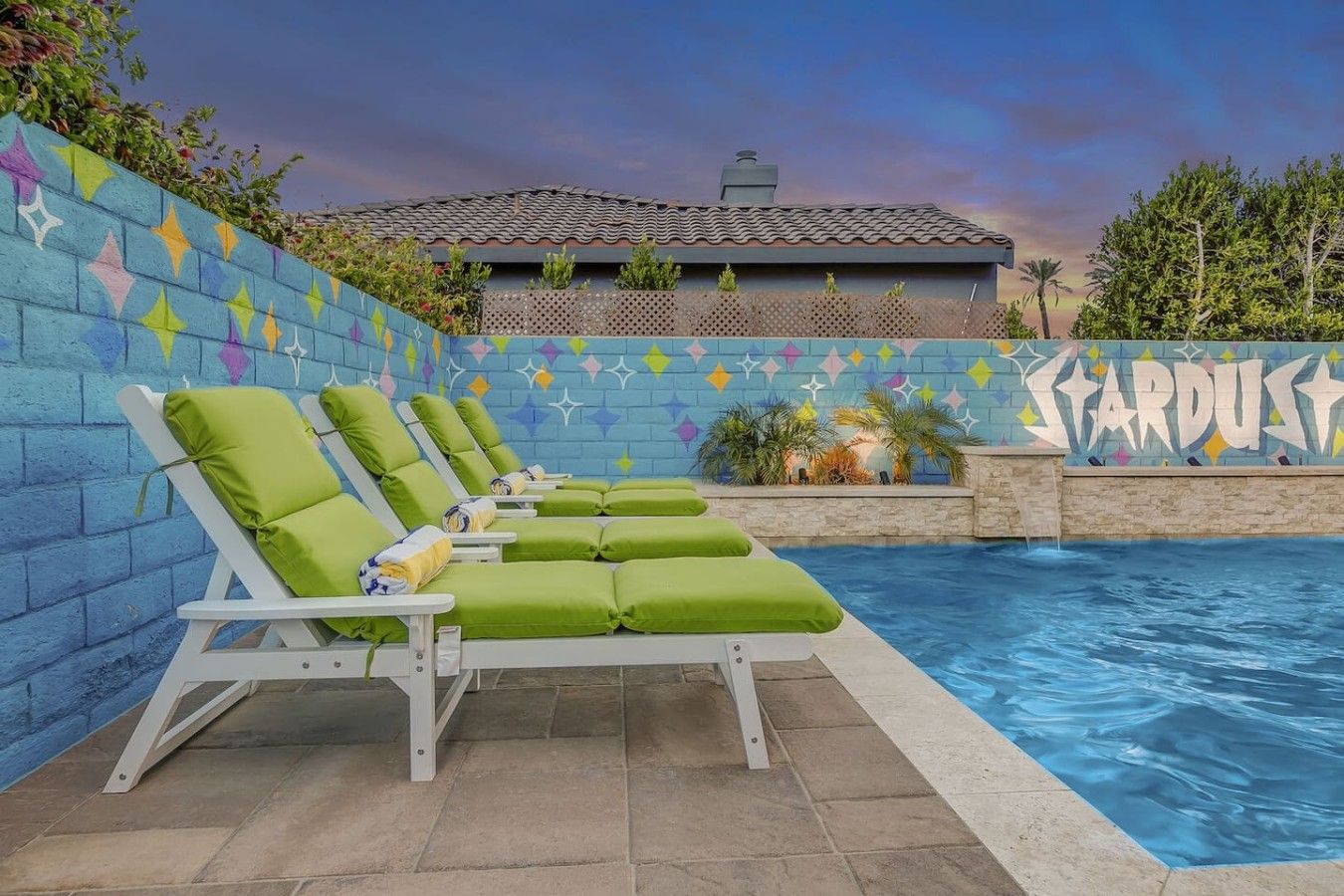 Zona de piscina con sillas de descanso y una pared decorativa.