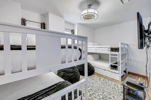 A dormitory room with bunk beds, a ceiling fan, a television, and a small table.