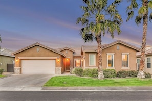 A residential house with a garage, a well-maintained lawn, and palm trees. - Stardust: Pool, Spa, FirePit, BBQ, EV Charger! (Indio)