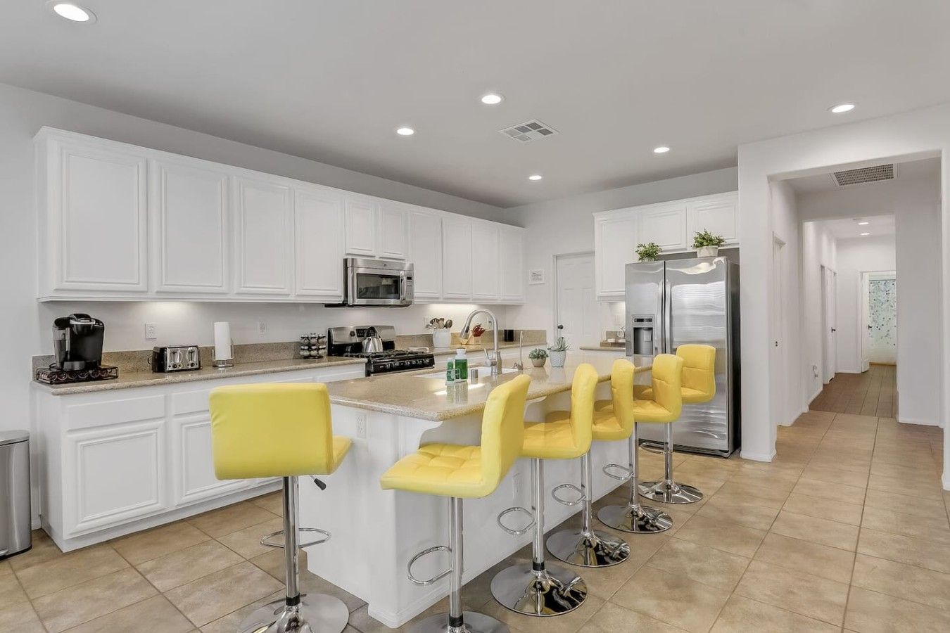 Una cocina moderna con armarios blancos, electrodomésticos de acero inoxidable y taburetes de bar amarillos.