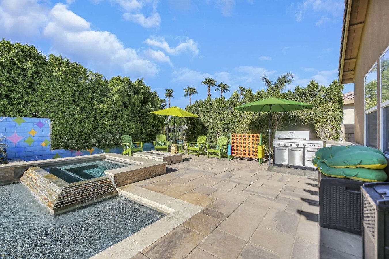 An outdoor patio with a pool, green chairs, a grill, and umbrellas.