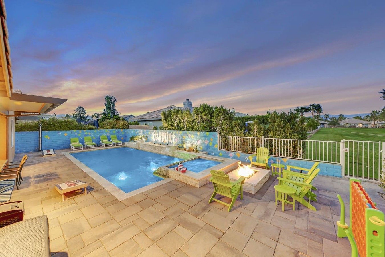 A swimming pool with a fire feature, surrounded by green chairs and a paved deck.