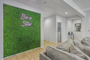 A room with a green wall, a sofa, and a door leading to a laundry area. - Stardust: Pool, Spa, FirePit, BBQ, EV Charger! (Indio)