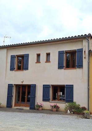 A two-story building with blue shutters, a small balcony, and potted plants. - BOYER BAS COTTAGE (2–10 people) With Private Pool (Saint-Gaudéric)
