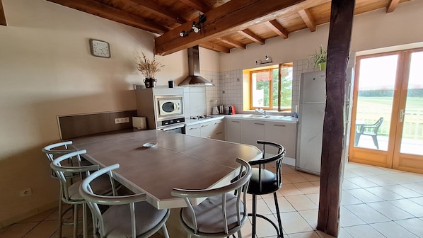 Une cuisine dotée d’un grand îlot central, de meubles blancs et d’une fenêtre donnant sur un jardin.