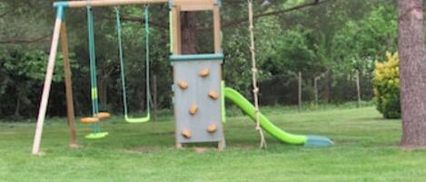 Une aire de jeux avec des balançoires, un toboggan et des prises d’escalade.