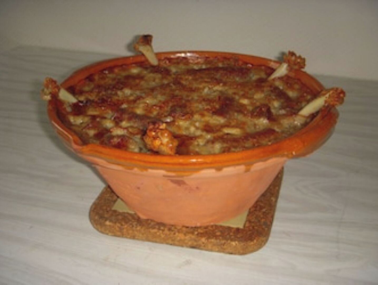 Un plat de ceràmica amb una cassola al forn, possiblement amb carn i verdures, col·locat sobre un suport.