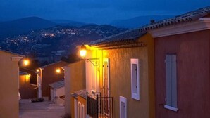 A narrow street with buildings on either side, leading to a brightly lit entrance. - Welcoming and comfortable T2 house in Fayence (Fayence)