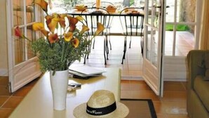Un espace repas ouvert avec une table dressée pour deux personnes, un vase de fleurs et un chapeau posé sur la table.