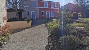 Un immeuble résidentiel avec une allée en gravier menant à la porte d’entrée, entouré de végétation et sous un ciel dégagé.