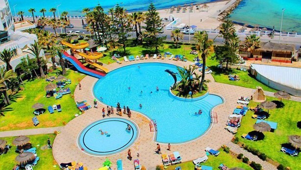 Un resort con una amplia piscina central, un tobogán acuático y una zona de playa.