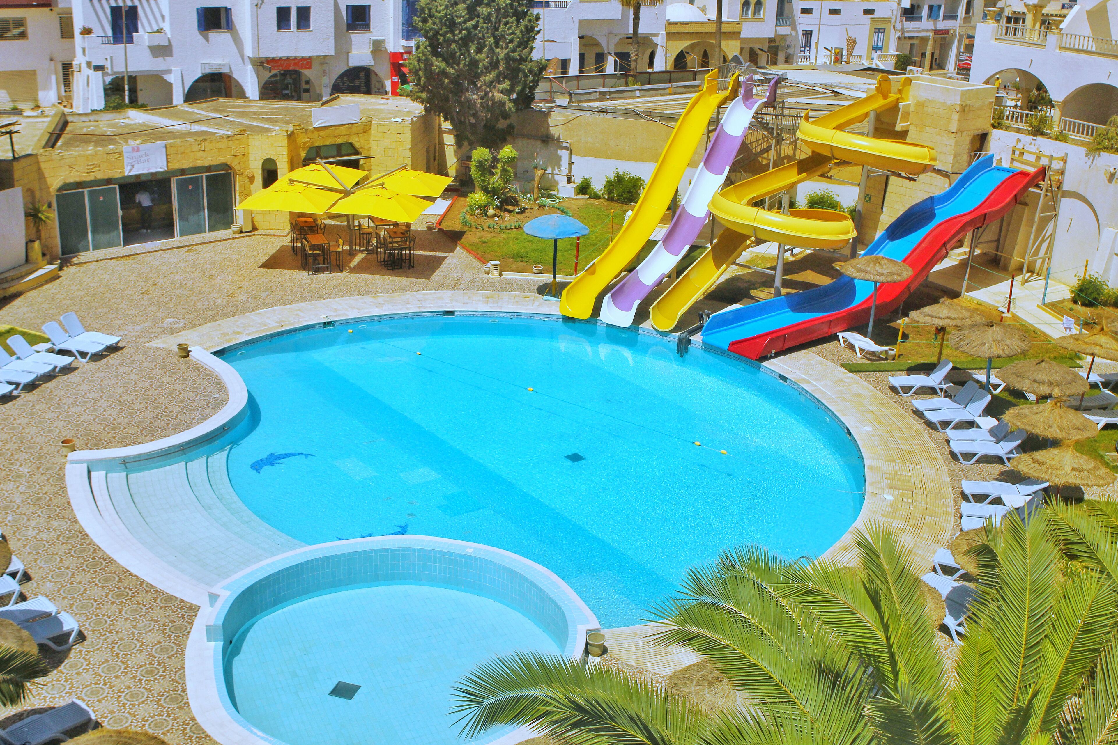 Ein großer Pool mit mehreren Wasserrutschen, umgeben von Liegestühlen und Sonnenschirmen.