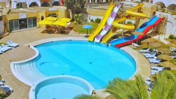 Ein großer Pool mit mehreren Wasserrutschen, umgeben von Liegestühlen und Sonnenschirmen.