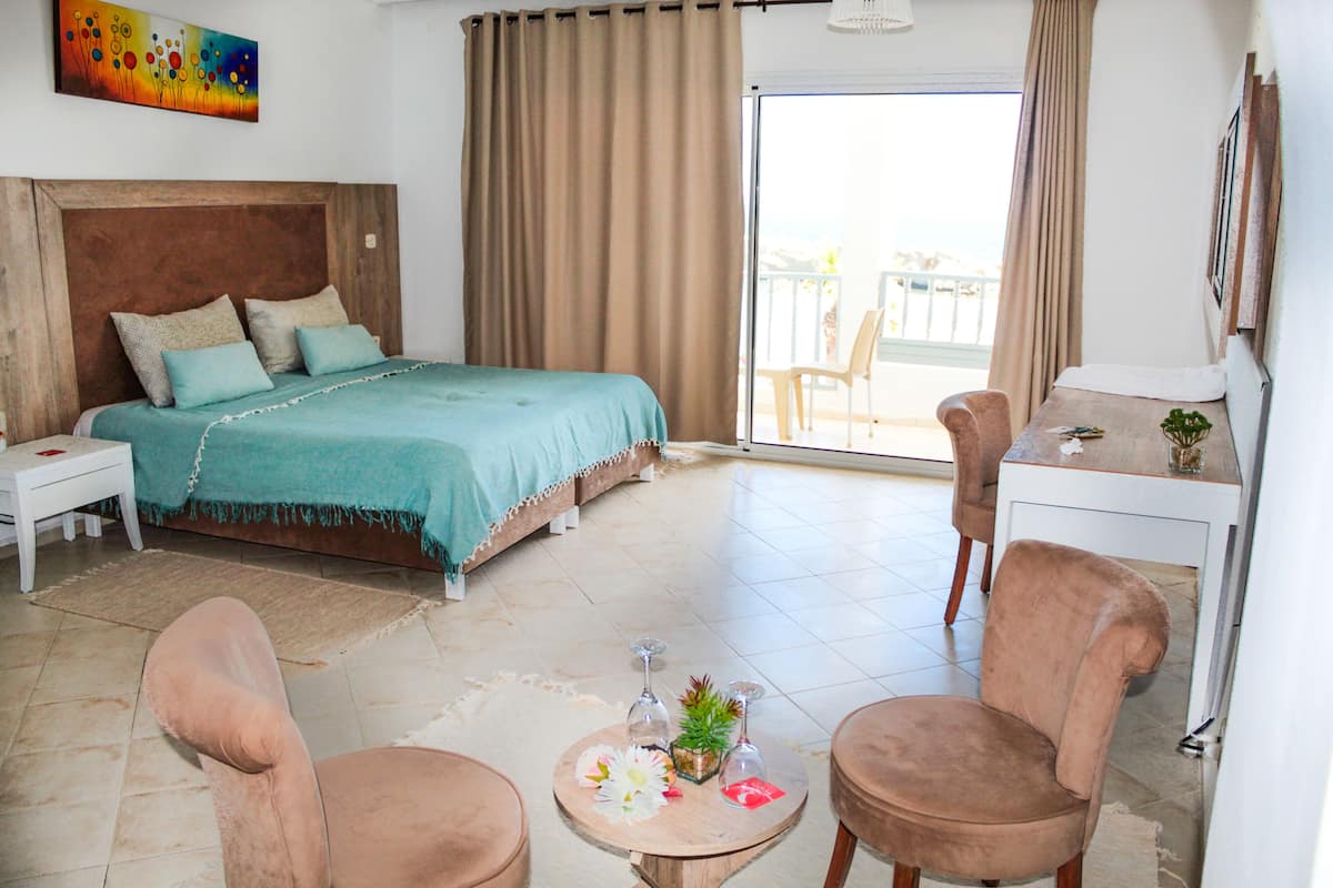A bedroom with a bed, two chairs, a small table with a vase, and a desk with a chair.